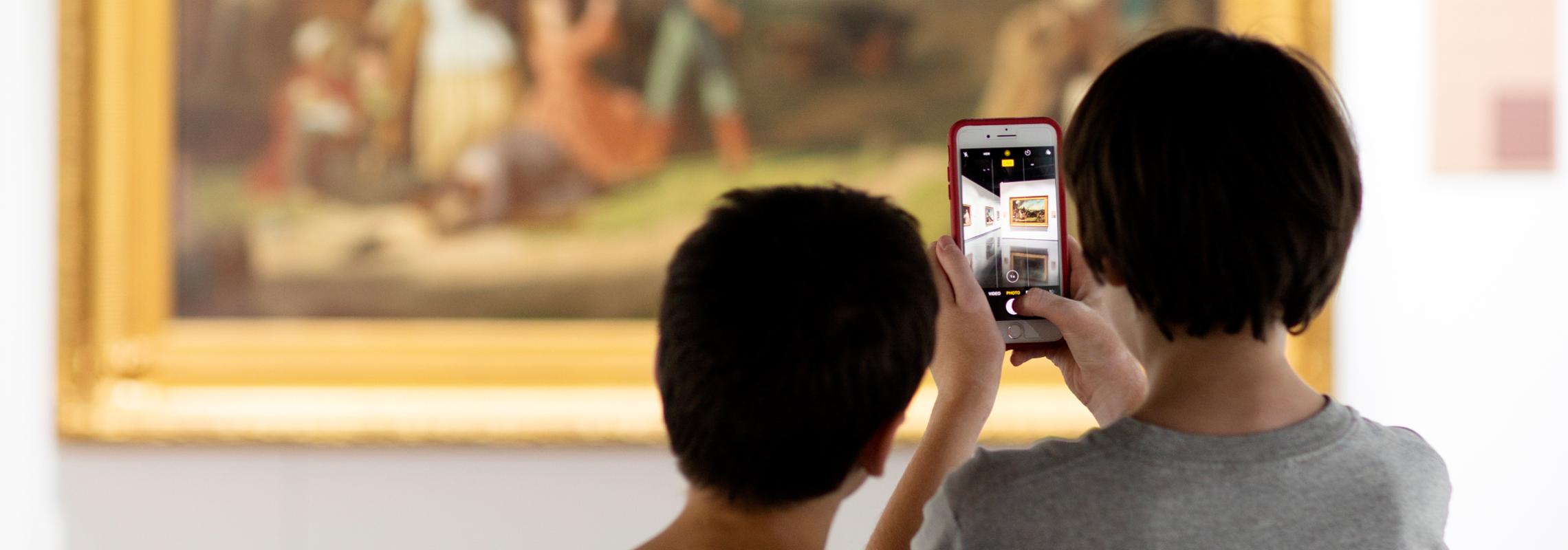 Two boys photograph a painting