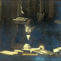 University of Missouri Journalism professor Frank Martin, writing in a book at his desk, ca 1912.