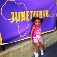 Young Black girl in front of a purple and yellow Juneteenth KC banner