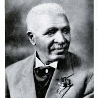 Head and chest studio shot of Black man with mustache and gray hair in a suit 
